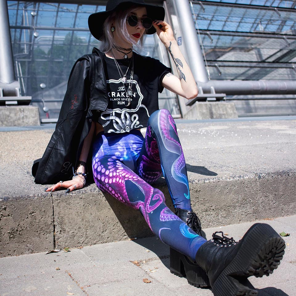 Woman wearing printed octopus leggings and black hat, boots and jacket.